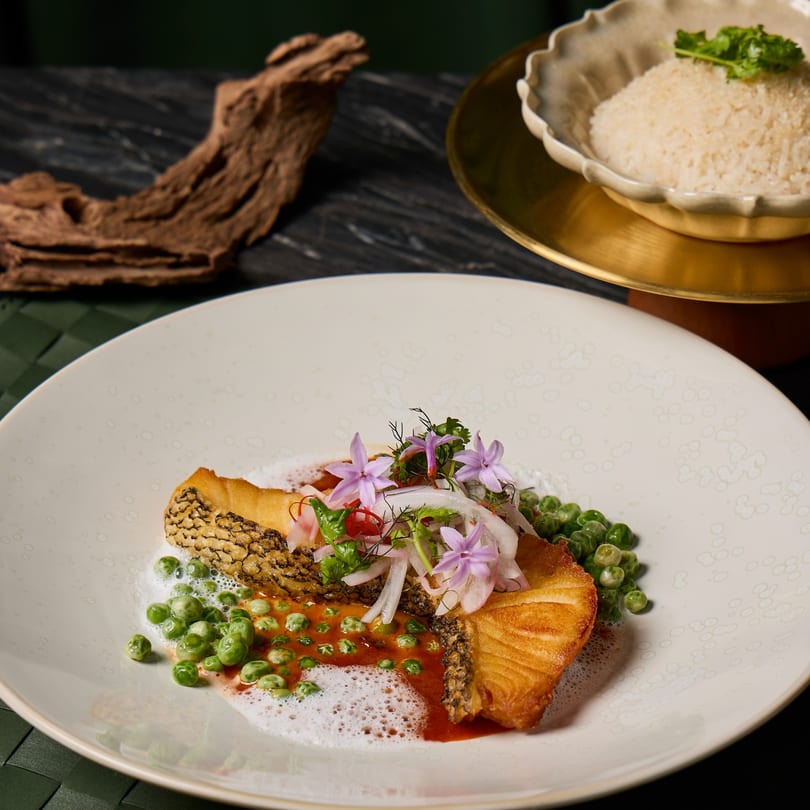 Crispy Thai fish with green peas, red sauce, and edible flowers, served with a side of rice.