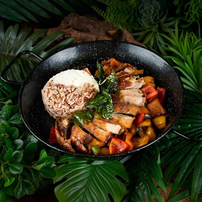 Khaosan's Thai dish with sliced chicken, colorful vegetables, and rice in a black pan.