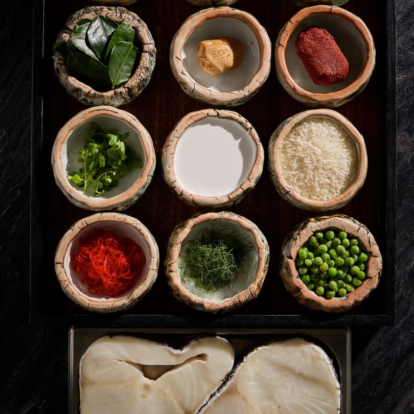 Overhead view of Thai ingredients in small bowls, including kaffir lime leaves, curry paste, and fish.