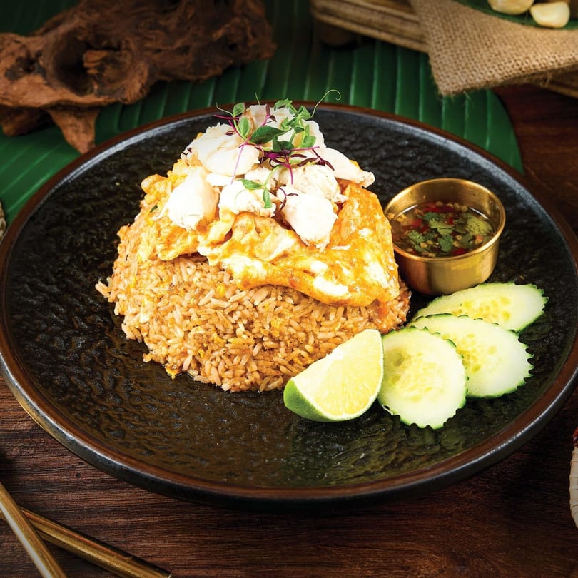 Khaosan's Thai crab fried rice with egg, lime, cucumber, and dipping sauce on a dark plate.